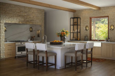 Natural stone walls and wood ceiling beams add vintage character to a modern kitchen.